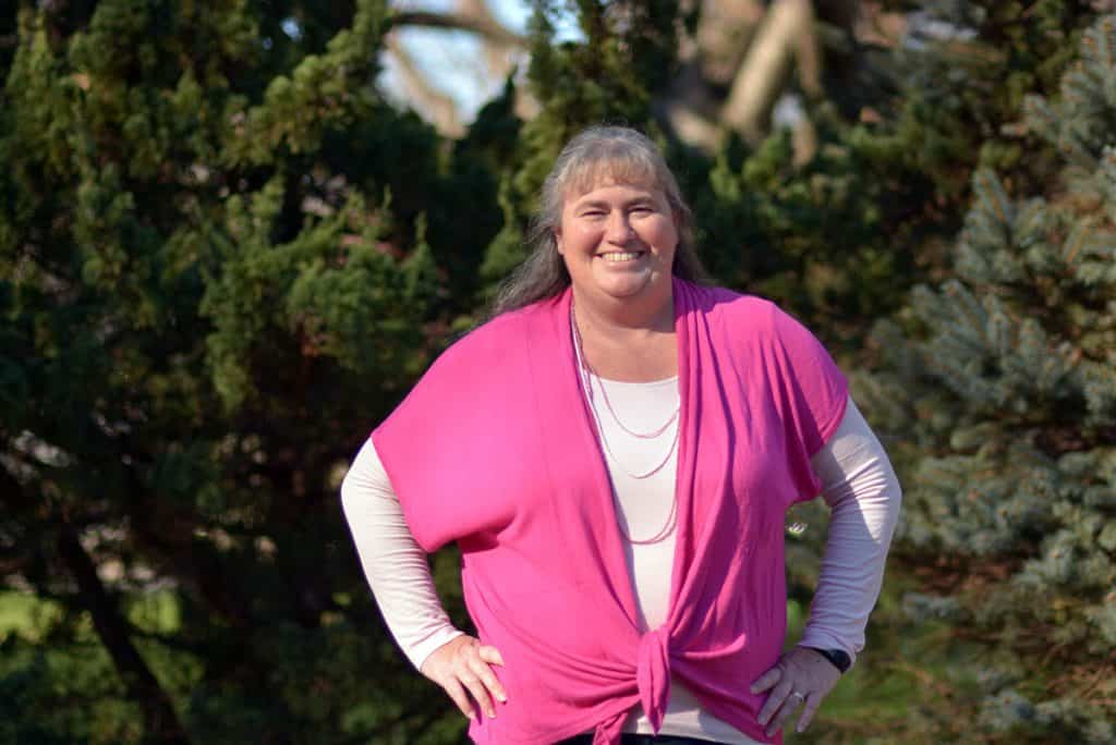woman in pink sweater standing in front of pine trees